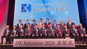 DXセレクション2026の表彰式で『優良事例』として表彰され、賞状を受け取り掲げる社長の様子