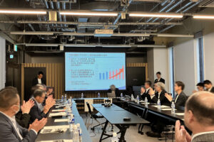 発表後、前方に立つ登壇者の旭光電機　代表取締役社長　和田に向けて、会場の参加者たちが一斉に拍手をしている様子